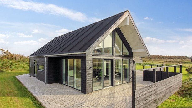 A modern house with a sloped roof, large glass windows, and a wooden deck.