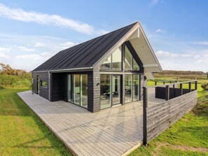Een modern huis met een schuin dak, grote glasramen en een houten terras.