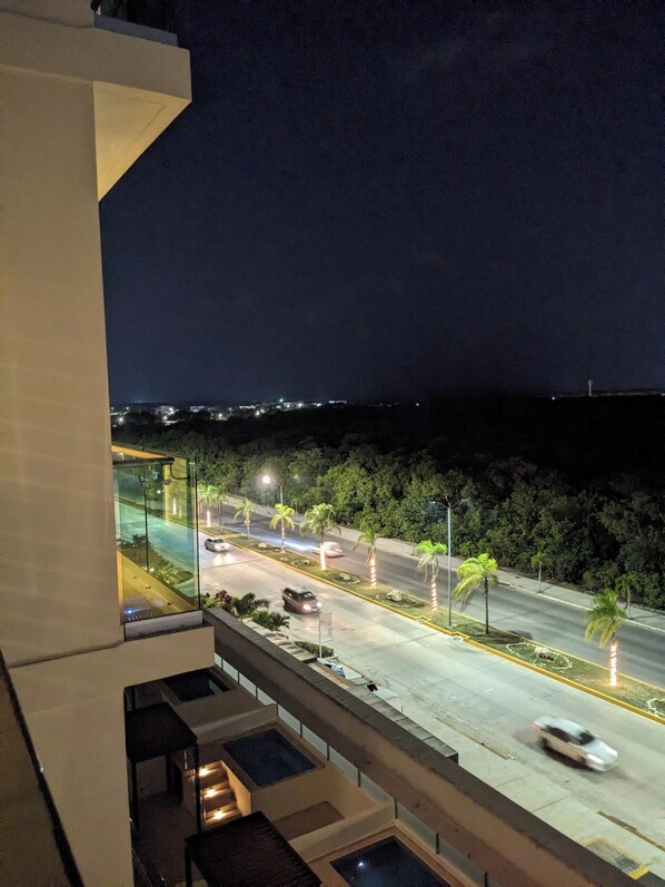 Vista nocturna desde un balcón sobre una calle con palmeras y farolas.
