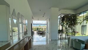 Een ruim, modern interieur met een lange receptiebalie, een zithoek met een bank en stoelen, en een groot raam met uitzicht op groen.