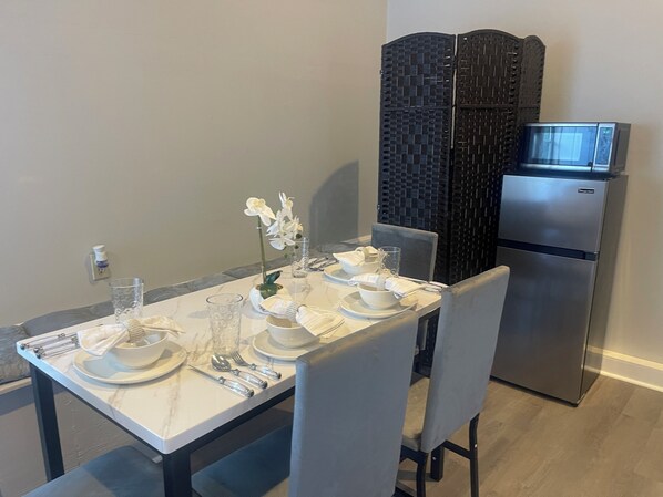 Un comedor con una mesa dispuesta para cuatro personas, un refrigerador y un separador decorativo.