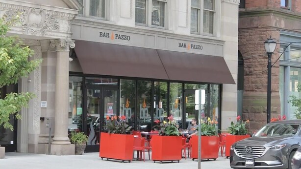 Un bar llamado BAR PAZZO con terraza y un coche estacionado cerca.