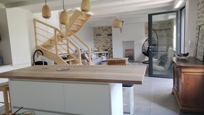 Une cuisine moderne dotée d’un îlot central, d’un escalier en colimaçon en bois et d’un coin repas avec une chaise noire.