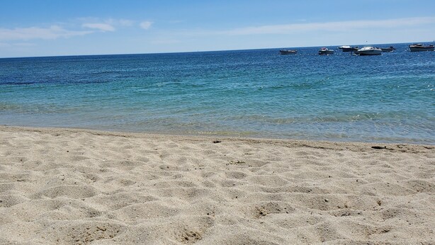 Une plage avec une eau d’un bleu limpide et des bateaux visibles au loin.