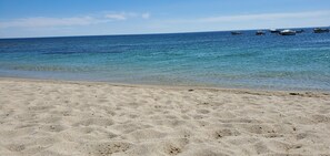 Une plage avec une eau d’un bleu limpide et des bateaux visibles au loin.
