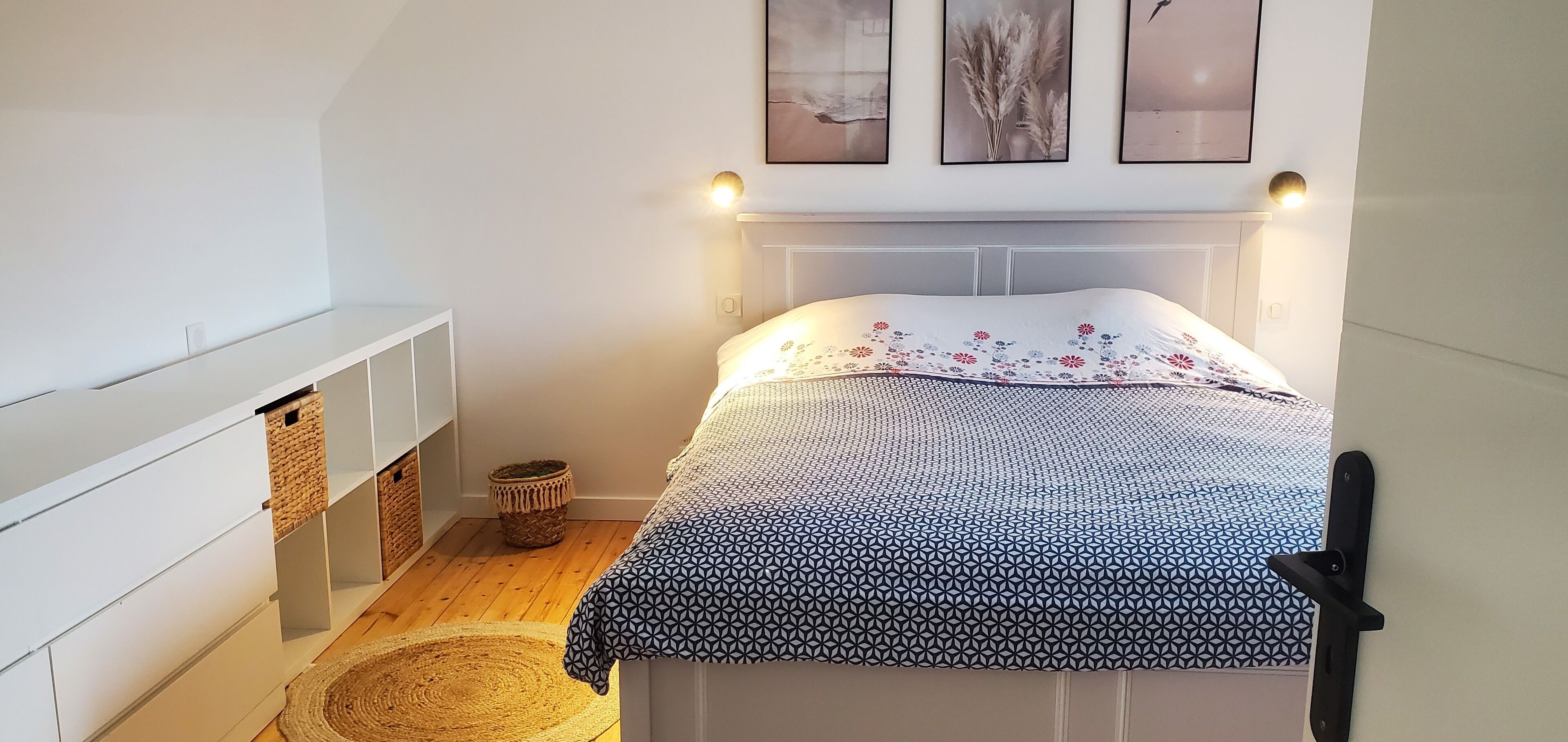 Un dormitorio con cama, mesita de noche, una alfombra pequeña y estante de pared.