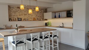 Une cuisine moderne avec un îlot central en bois, des tabourets de bar blancs, des luminaires suspendus et un pare-feu en pierre.
