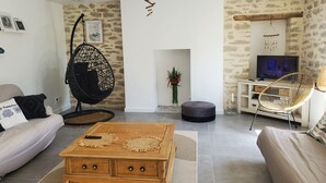 Un salon comprenant un canapé, une table basse en bois, un fauteuil suspendu, un téléviseur et un mur décoré d’un motif imitant la pierre.