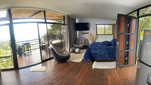 A modern bedroom with a large window, a flat-screen TV, a sofa, and a bed.