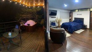 A bedroom with a bed, a TV, and a balcony with a hot tub.