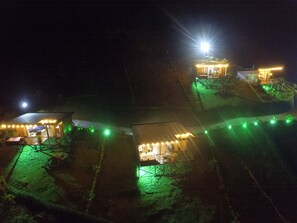 A series of small, illuminated cabins with outdoor seating areas, connected by a pathway. - Hermosa Cabaña Familiar con Jacuzzi y Cocina. El Mejor Paisaje de la Región (Guatape)