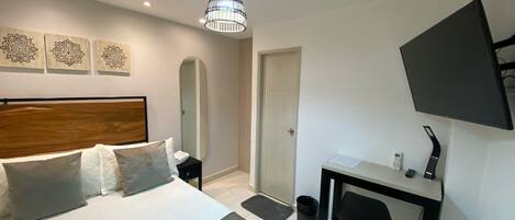 A bedroom with a bed, bedside table, mirror, desk with chair, TV, and decorative wall art.