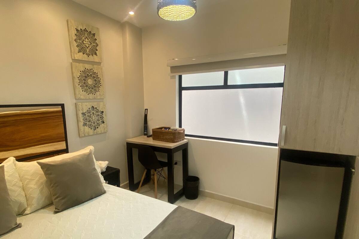 Une chambre avec un lit, un bureau, une chaise, une fenêtre et un réfrigérateur.