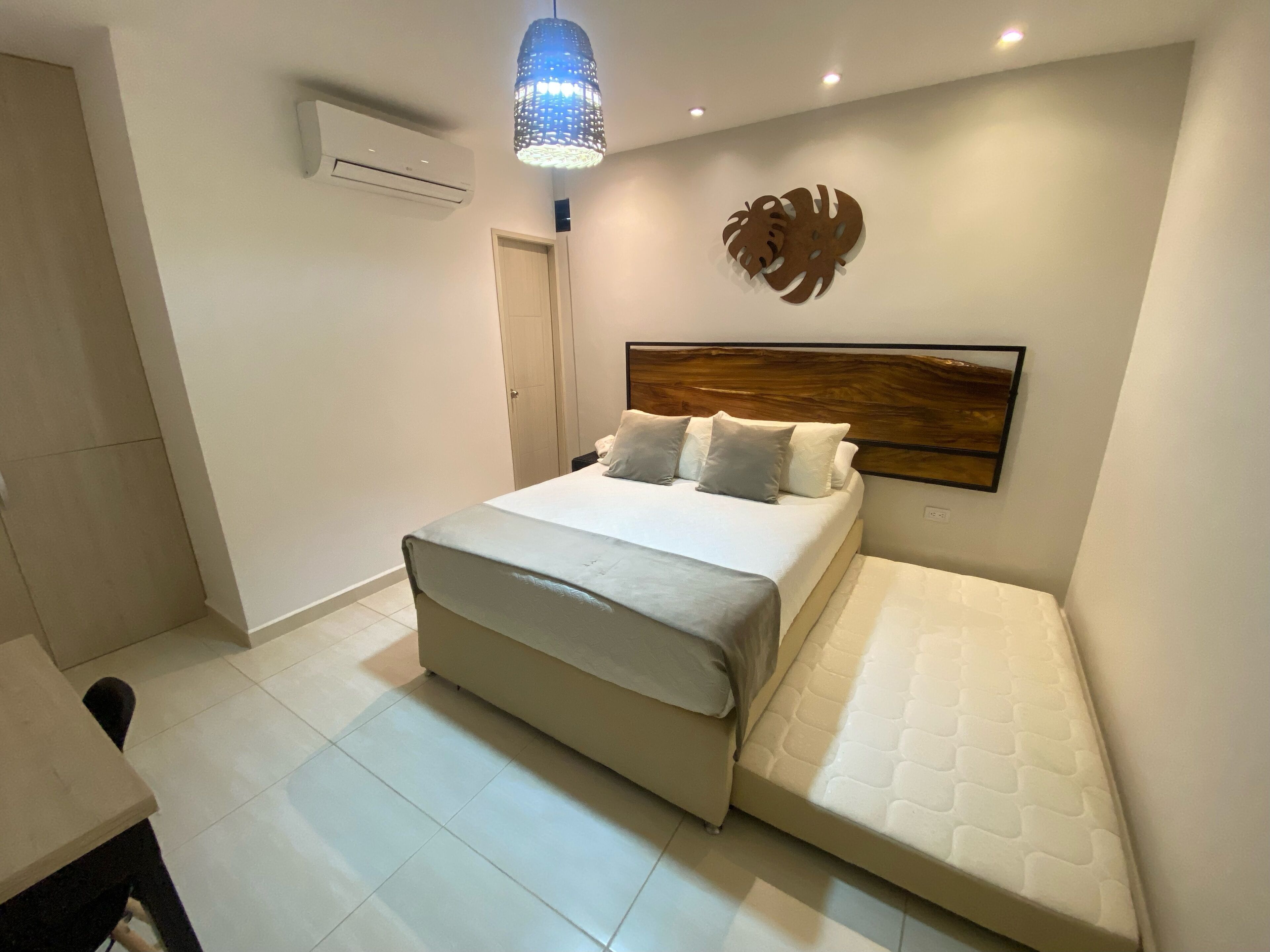Un dormitorio con cama, mesita de noche, aire acondicionado mural, un adorno en la pared y una lámpara de techo.