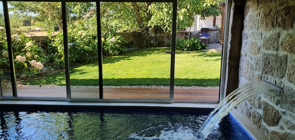 A pool with a waterfall feature, surrounded by a stone wall and a wooden deck.