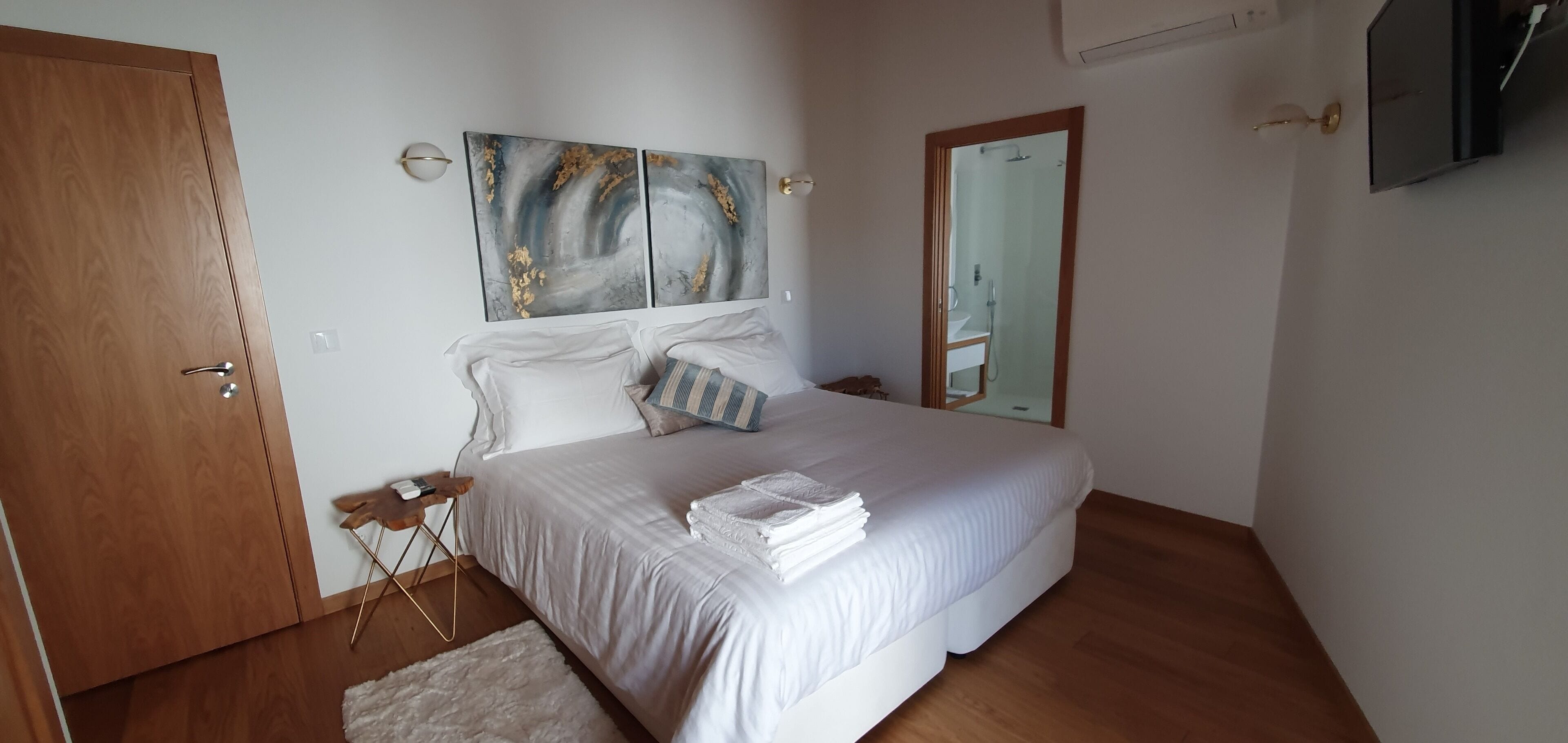 A bedroom with a large bed, a wooden door, a mirror, and a wall-mounted artwork.