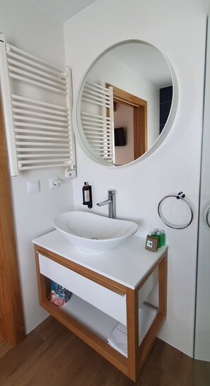 Un baño con lavamanos blanco, espejo redondo, toallero y armario de madera.