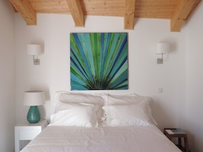 Een slaapkamer met een bed, witte lakens, een groene lamp en een schilderij aan de muur.