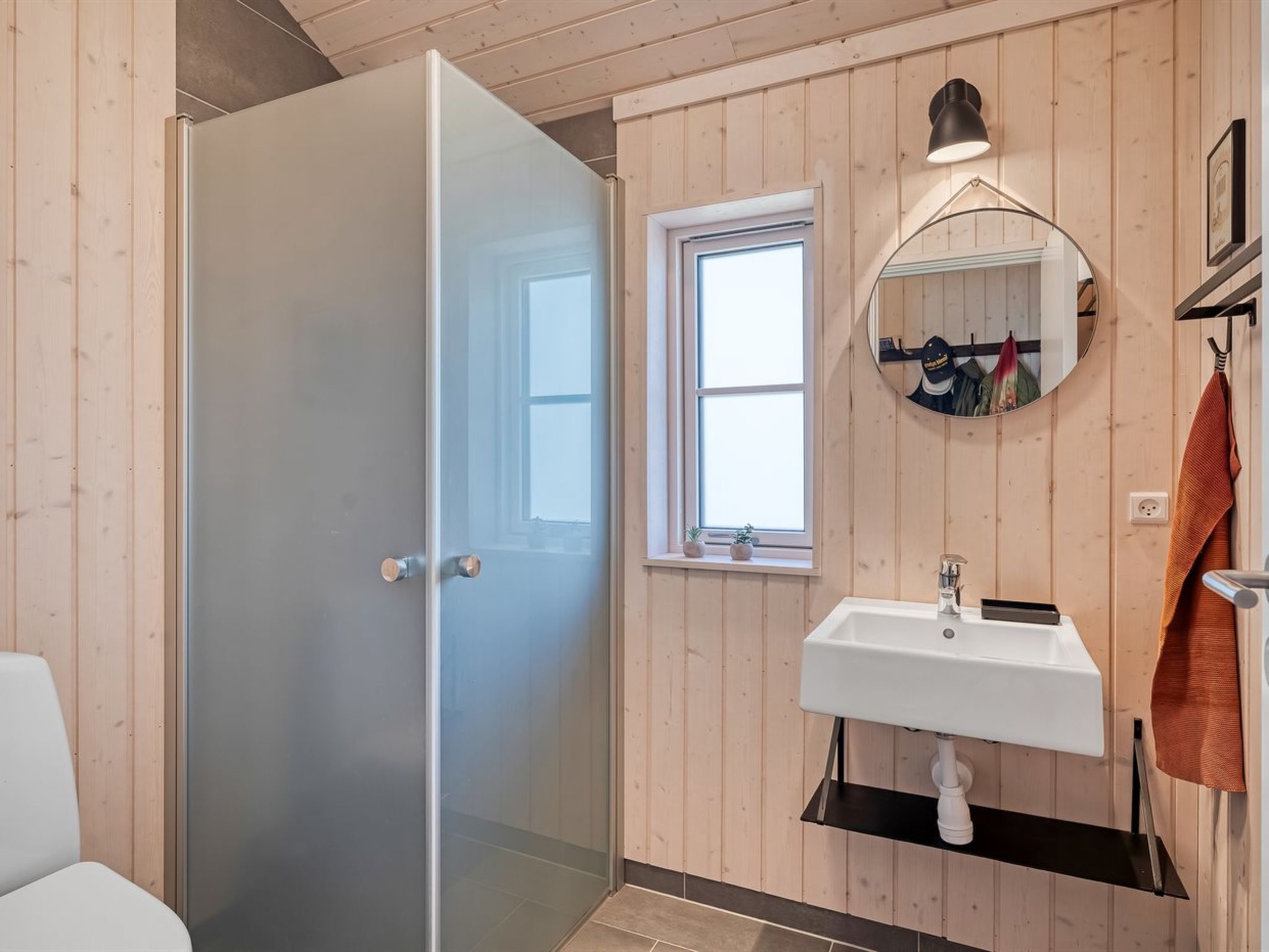 Un baño con mampara de vidrio, lavamanos blanco, espejo y paredes de madera.
