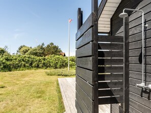 Une terrasse en bois avec une rambarde en métal, un mât pour drapeau et un ciel dégagé.