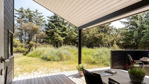 A wooden deck with outdoor furniture, a potted plant, and a view of a forested area.