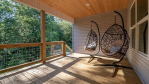 A wooden deck with a railing, two hanging chairs, and a view of trees. - "THE ODIN" off the OZ TRAIL (Bella Vista)