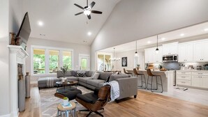 A spacious living area with a large sofa, a coffee table, and a TV mounted on the wall. There is a kitchen area with white cabinets and a microwave. - "THE ODIN" off the OZ TRAIL (Bella Vista)
