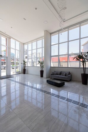 A spacious lobby with large windows, a grey sofa, and potted plants. - Contemporary Studio - GRU (Centro Guarulhos)