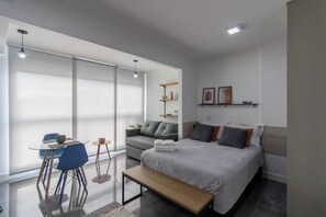 A modern bedroom with a bed, bedside tables, a sofa, and a dining area with chairs. - Contemporary Studio - GRU (Centro Guarulhos)