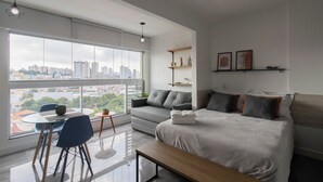 Et moderne hotelværelse med et stort vindue, en seng, en sofa, et spisebord med stole og et lille sofabord.