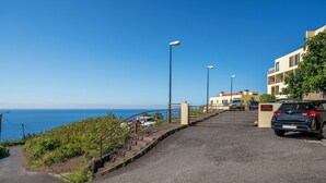 Eine Küstenstraße mit Parkplatz, einer Treppe zu einem Gebäude und freiem Blick auf das Meer.