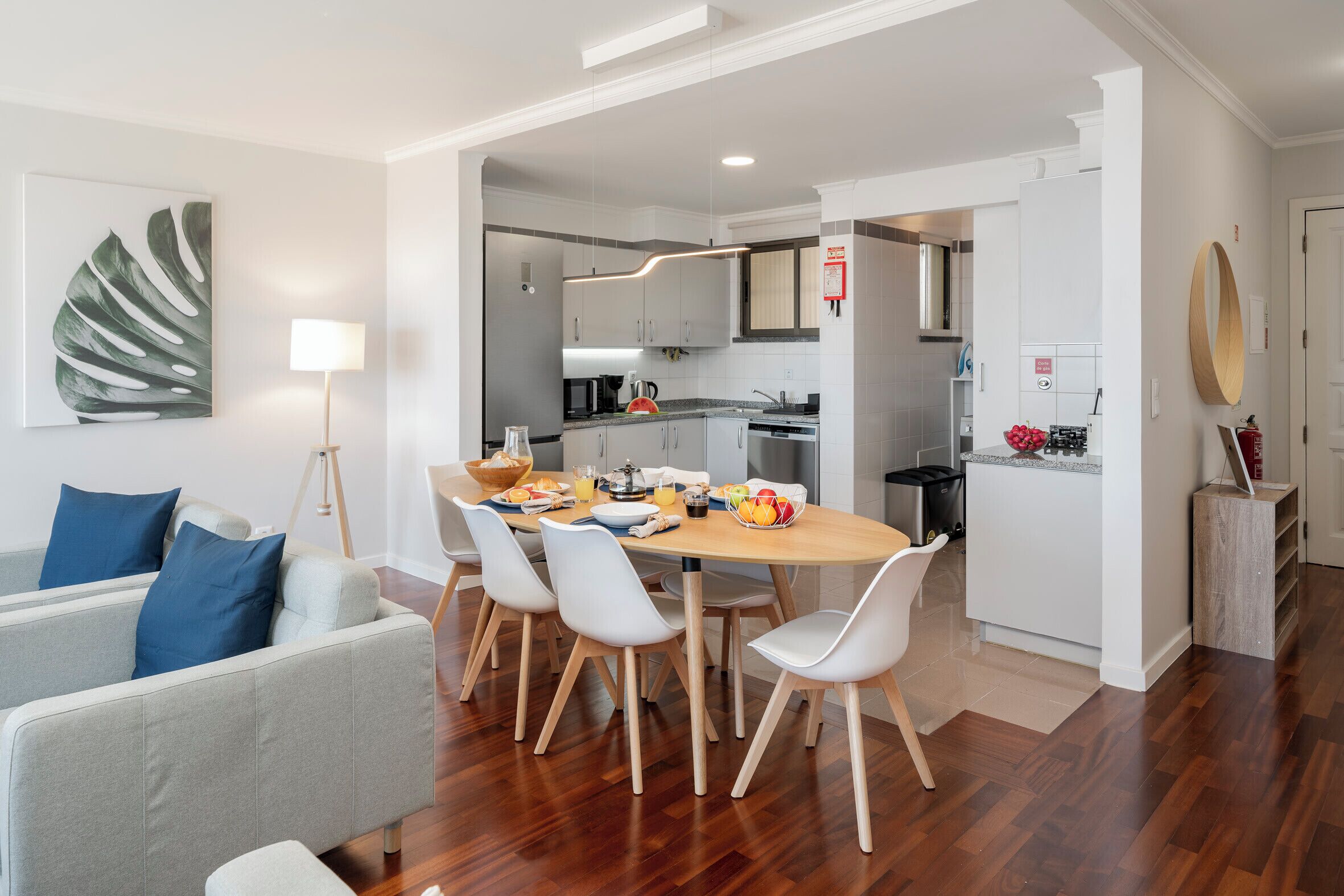 Ein modernes Wohnzimmer mit einem grauen Sofa, weißen Stühlen und einem Esstisch, gedeckt für das Frühstück.