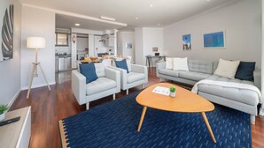 Ein modernes Wohnzimmer mit einer Couch, Sesseln und einem Couchtisch. Im Hintergrund befindet sich eine Küche mit einem Essbereich.