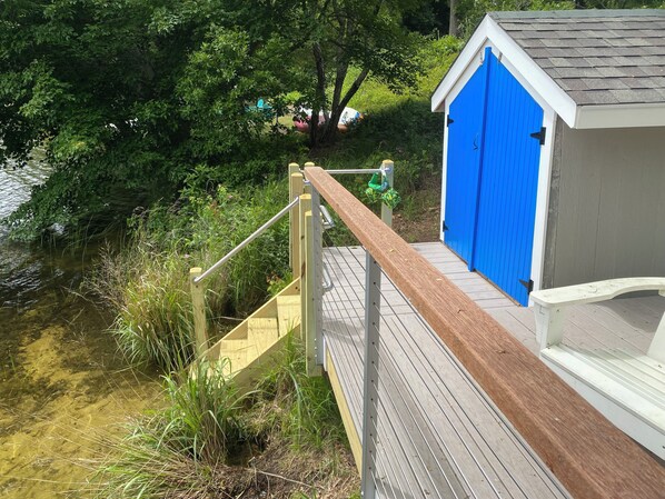 A wooden deck with a metal handrail leading to a blue building with a white roof.