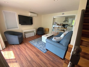 A living room with a blue sofa, a grey armchair, a coffee table, and a TV mounted on the wall.
