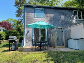 A house with a patio area featuring a table and chairs under a green umbrella, a barbecue grill, and a wooden fence. - Lakefront retreat w/ deck, dock, sandy beach, 4 watercraft, <6 mins to 2 beaches (Orleans)