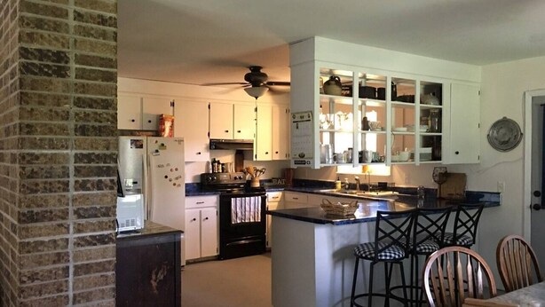 A kitchen with a brick wall, a central island with bar stools, white cabinets, and a ceiling fan. - Great get away to a country home with large yard and outdoor sitting area.  (Rose Bud)