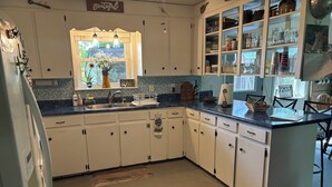 A kitchen with white cabinets, a blue countertop, and a window with a view of greenery. - Great get away to a country home with large yard and outdoor sitting area.  (Rose Bud)