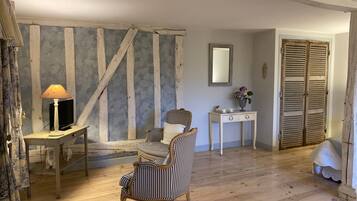 A rustic room with exposed wooden beams, a wooden floor, a striped armchair, a small table with a lamp, a TV, and a mirror.