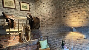 A rustic room with a brick wall, leather boots, and a wooden chair. - Domaine de la creuse (Moussey)