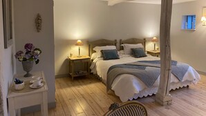 A bedroom with a large bed, two bedside tables with lamps, a small table with a vase of flowers, and a wooden chair. - Domaine de la creuse (Moussey)