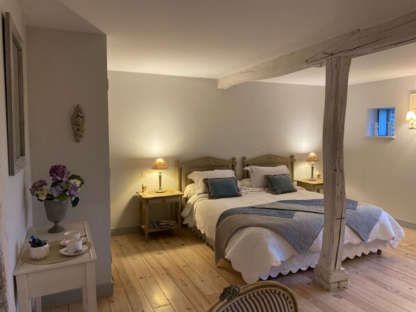A bedroom with a large bed, two bedside tables with lamps, a small table with a vase of flowers, and a wooden chair.