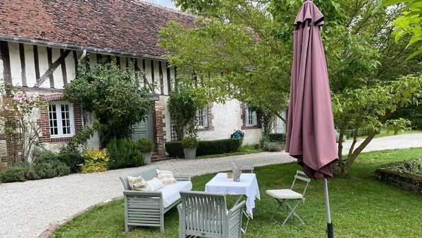A courtyard with a table and chairs, a covered umbrella, and a building with a tiled roof. - Domaine de la creuse (Moussey)