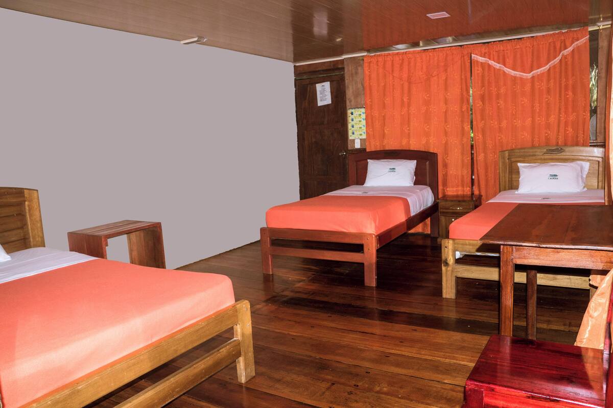 A room with two wooden beds, a wooden table, and a small wooden stool.