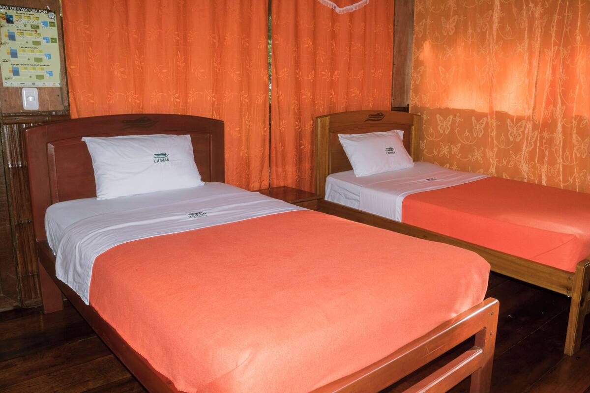 Two single beds with wooden frames and white bedding, orange curtains, and a wooden floor.