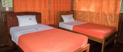 Two single beds with wooden frames and white bedding, orange curtains, and a wooden floor.