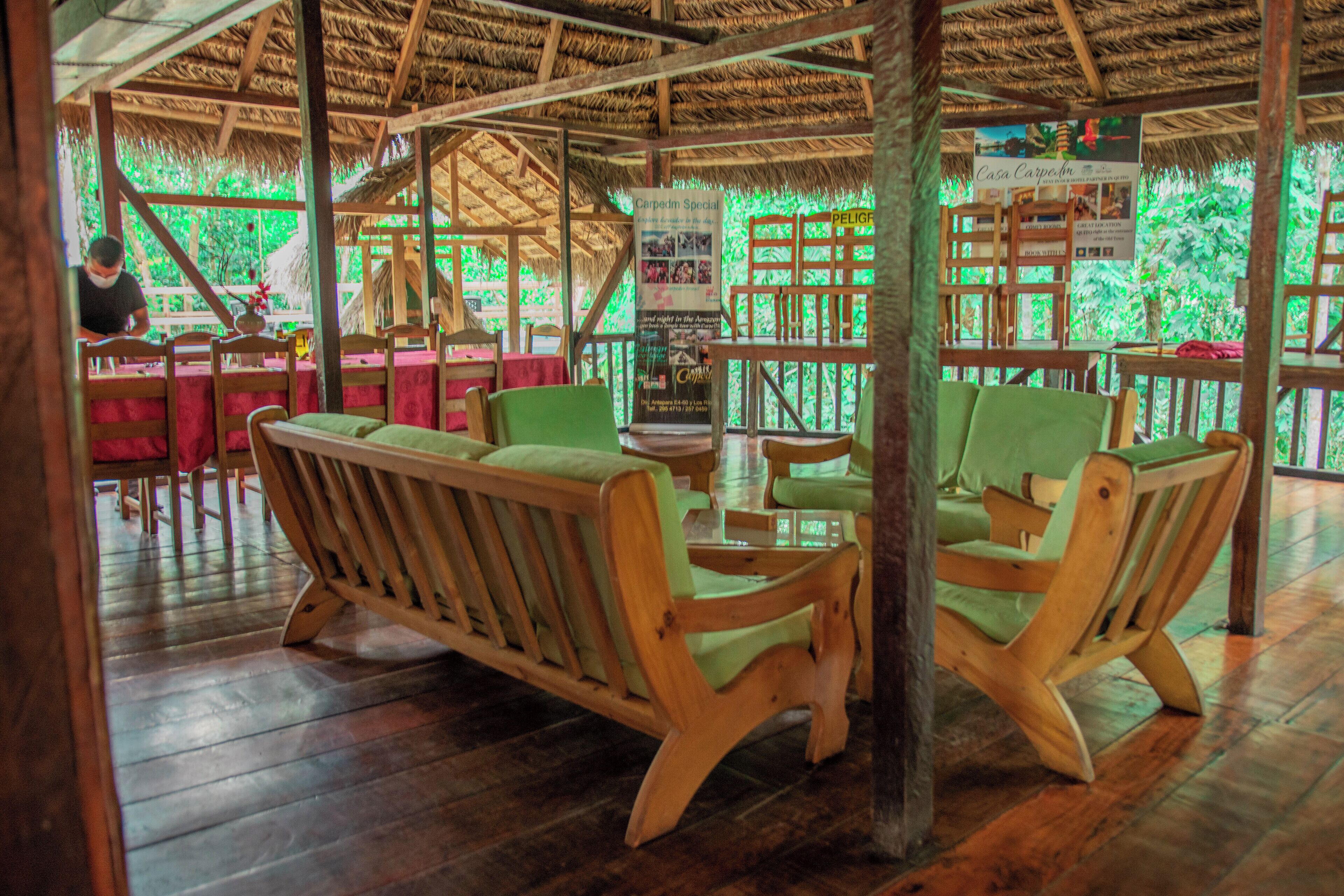 A wooden interior with thatched roof, wooden furniture, and a view of greenery outside.