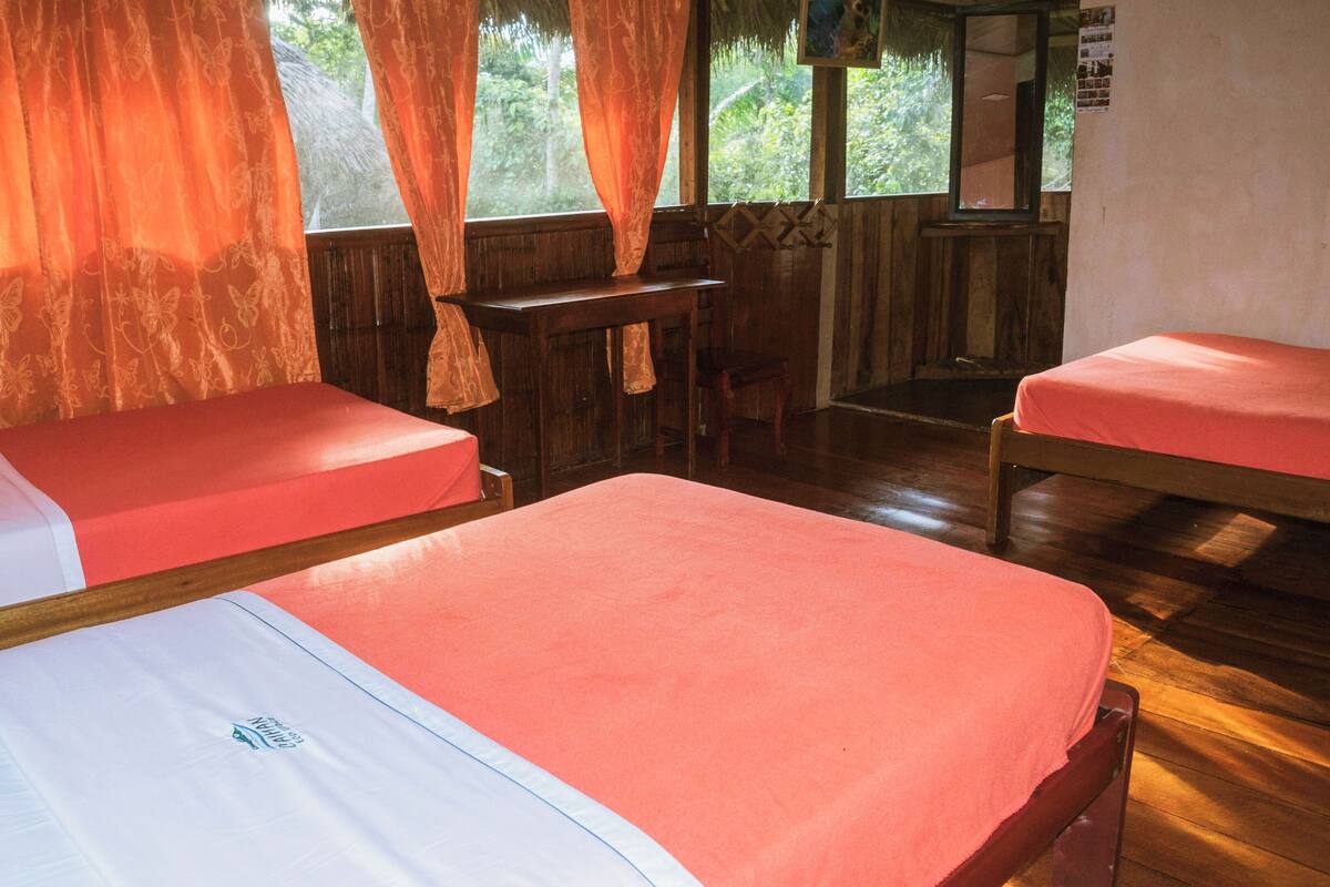 A room with two beds, a wooden desk, and a window with curtains.