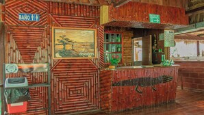 Zona de bar rústica con diseño de madera, un cuadro y un letrero que indica bar y salida de emergencia.