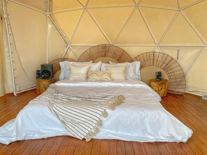 A bed with a white and beige striped blanket, a wooden headboard, and two speakers on wooden side tables.